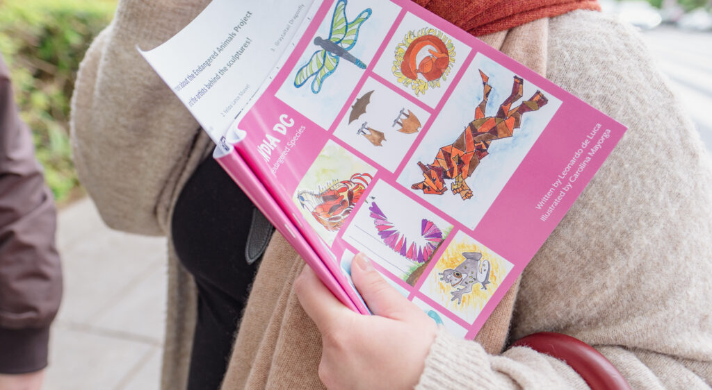 A person holds a pink coloring book with the drawings of many different animals on the cover