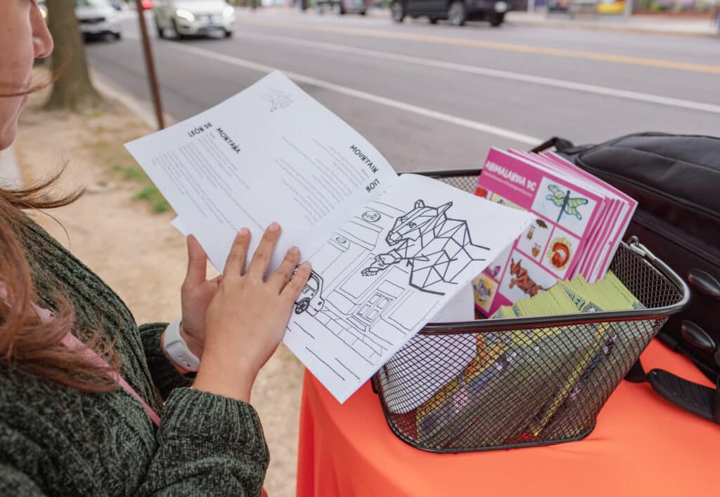 A woman on a street holds a coloring book open to a page with a large bobcat on it